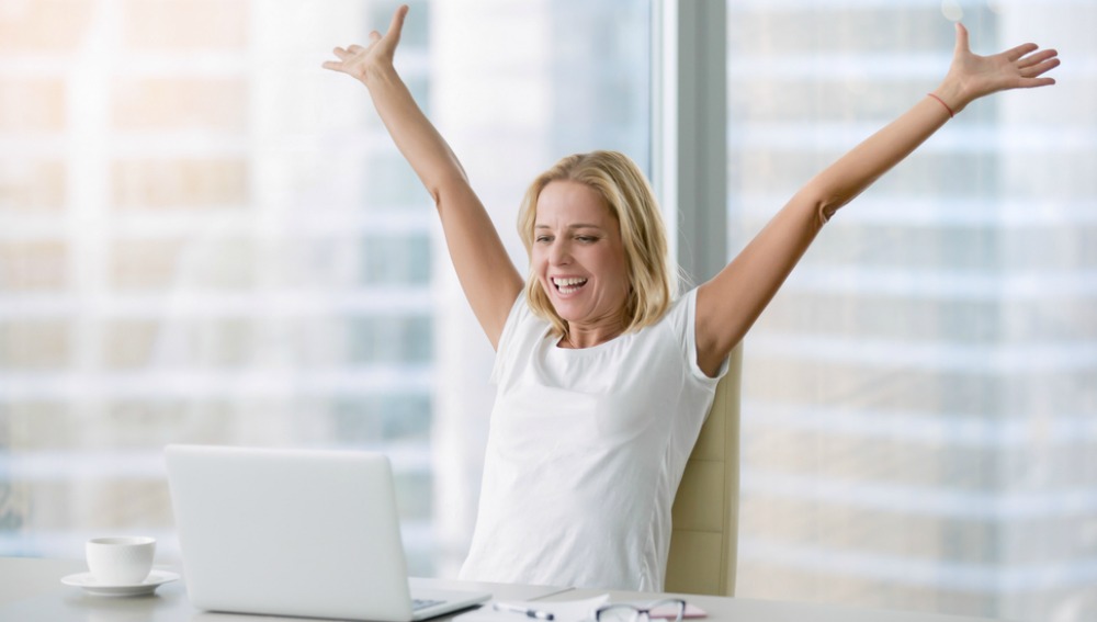Woman smiling and stretching her arms in front of a computer