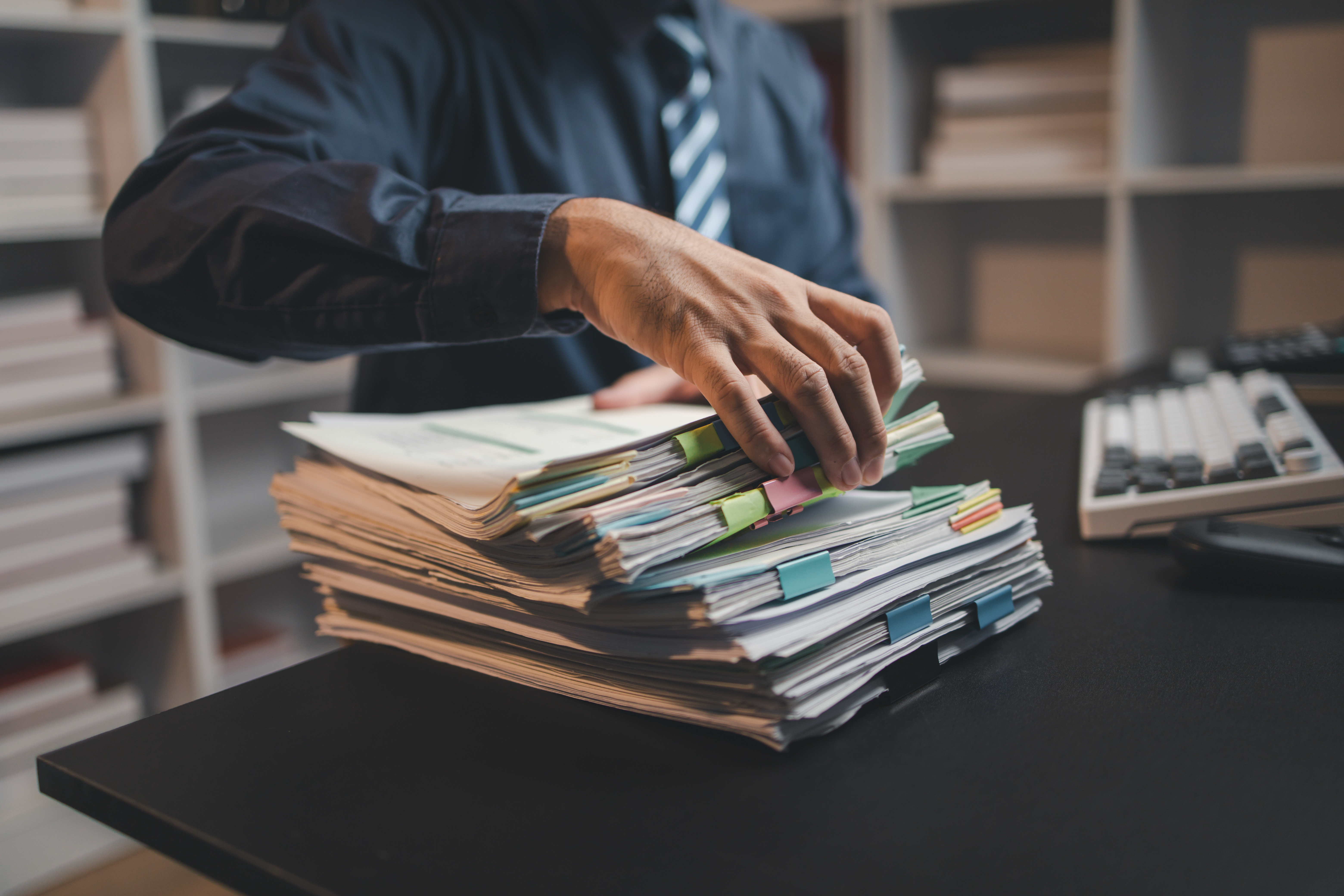 A man with his hand on a very large stack of paperwork, in need of document management solutions.