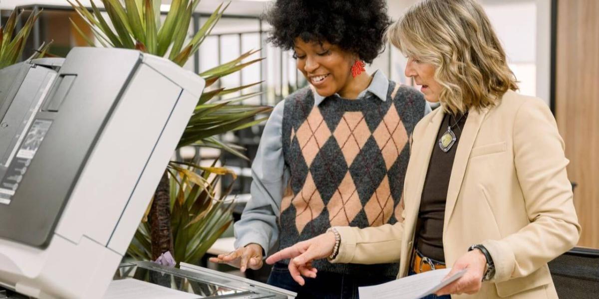 A professional office setting with employees using a multifunction printer or reviewing documents near shared office equipment
